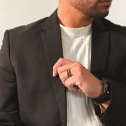 A man wearing a ceramic wood wedding ring with a black watch and a black coat.