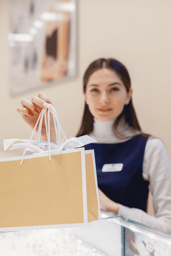 A jewelry store employee handing over shopping bags with a warm smile.