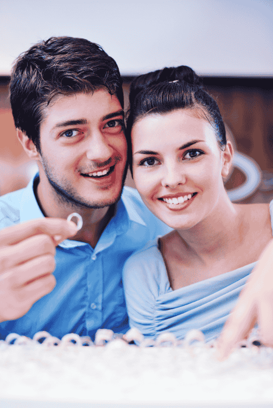 A smiling couple in a jewelry store holding an engagement ring.