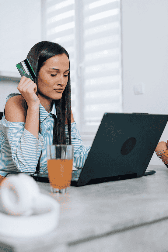 A woman making an online purchase with a credit card and laptop at a cozy workspace.