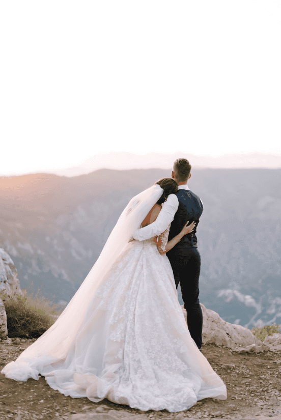 Bride and groom embracing on a mountain at sunset, wedding dress flowing.