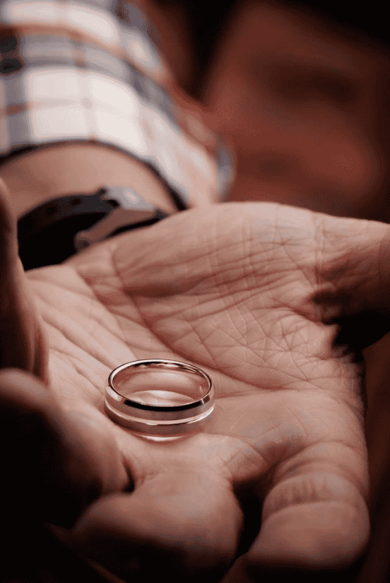 A close-up of a wedding band resting in the palm of a man's hand.