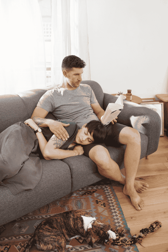 A Husband reading a book while Wife is sleeping on his lap.