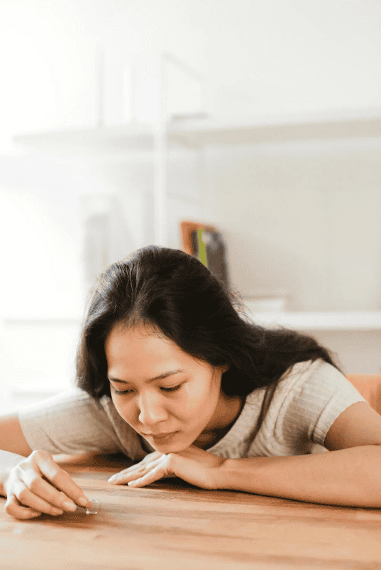 A sad woman resting her head on a table, staring at her wedding ring.