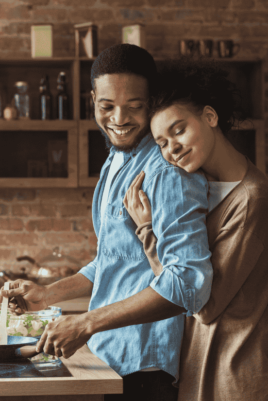 Husband is cooking while wife hugging him.